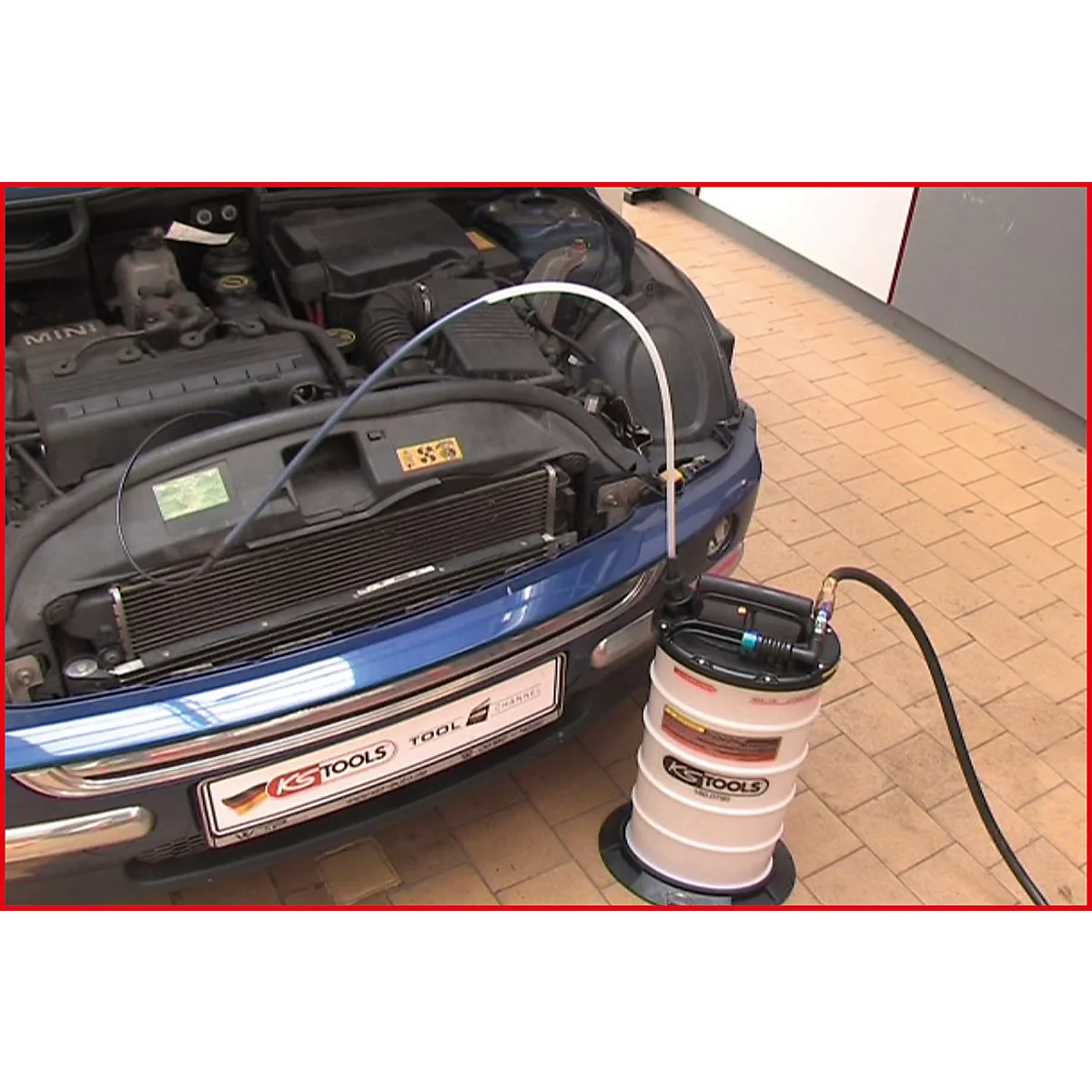 Motorraum eines blauen Mini, Ölwechsel mit KS-Tools Gerät. Schlauch führt zur Auffangvorrichtung.